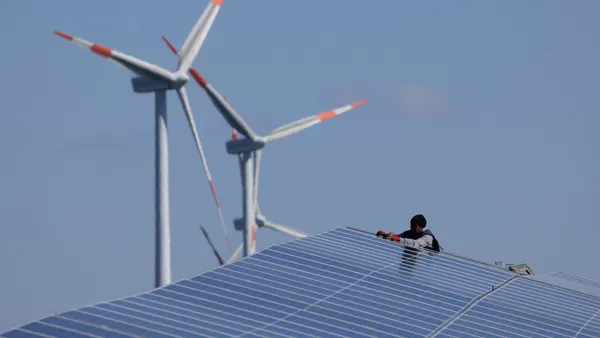 A worker installs solar panels at the construction site of a new solar energy park as wind turbines spin behind on April 06, 2023 near Prenzlau, Germany.