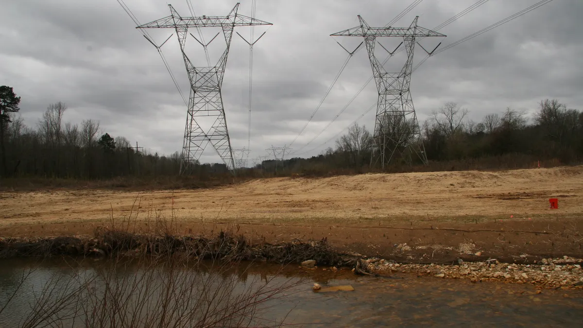 Electric transmission lines cross a creek with gray skies overhead.