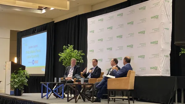 Three men are seated on a stage with a backdrop reading "Waste Today events" and "Corporate Growth Conference" behind them. One person in the center is speaking.