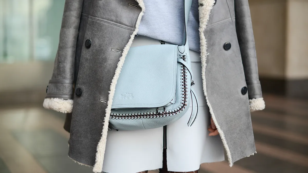 A closeup detail of a person's outfit, which includes a fur-lined coat and Coach bag.