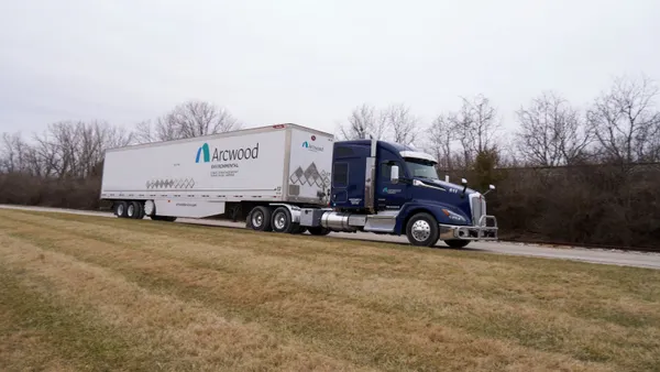 An 18-wheeler with Arcwood Envrionmental on its side is parked on a road, with brown grass in the foreground.