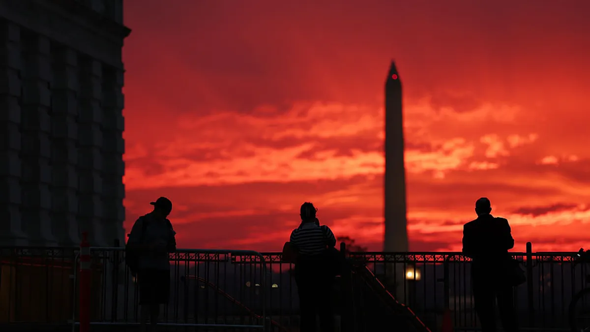 People are in the foreground looking toward the setting sun in the horizon and the Washington Monument.