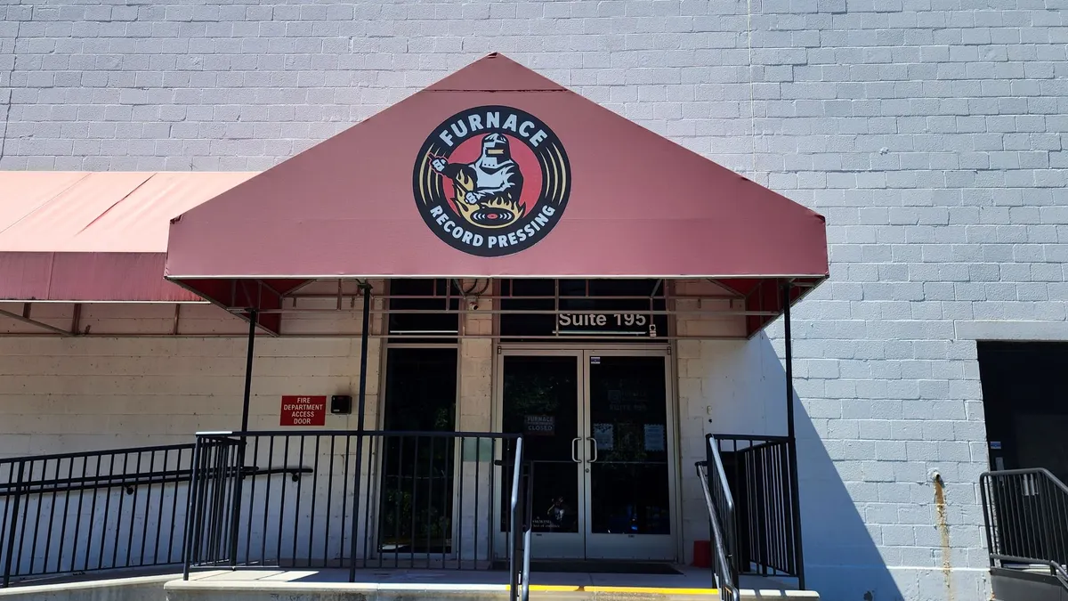 A faded red commercial canopy over a glass door entrance of a white building.