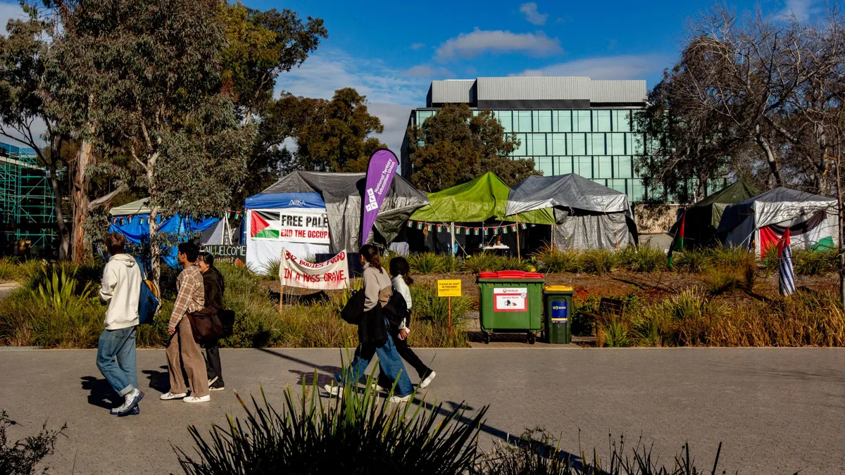 Tents situated on a college campus behind a walkway with people.