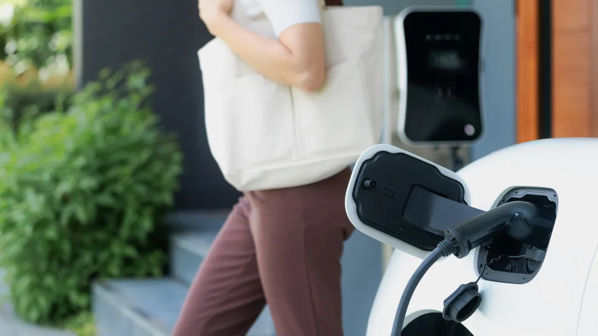 Focus image of electric vehicle recharging battery at home charging station with blurred woman walking in the background