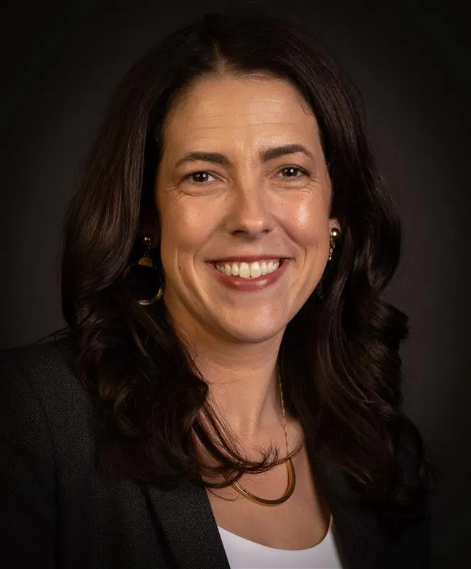 A person wearing a dark blazer and white shirt smiles for the camera