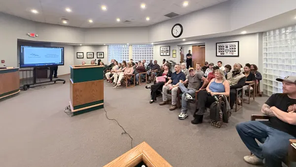 Many people seated in a large room with a podium and large TV screen.