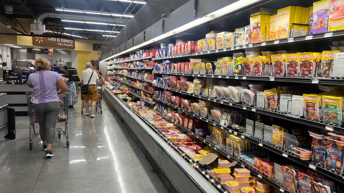 A rear view of multiple people pushing shopping carts next to a display case in a grocery store