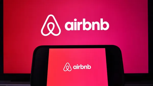 The Airbnb logo is displayed on a computer monitor and cell phone.