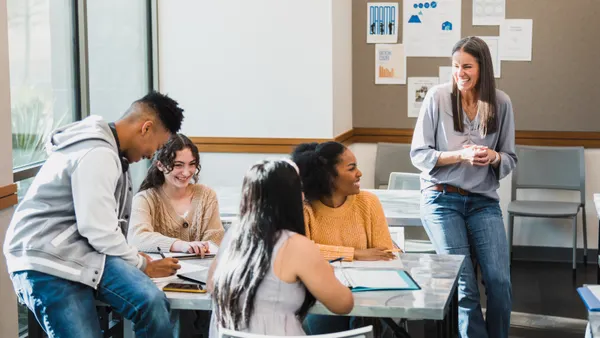A teacher engages with four teenage students seated at a table in a classroom.