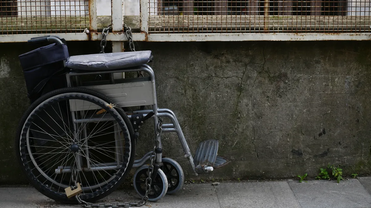 A battered wheelchair chained to a fence