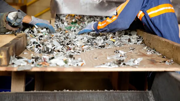 Two people in protective gear shift through various-sized pieces of metal on a wooden table. 