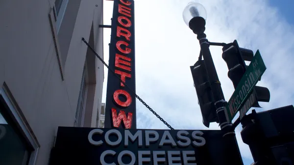 A white sign with black text reading 'Compass Coffee' in front of and below a lighted neon saying reading 'Georgetown'