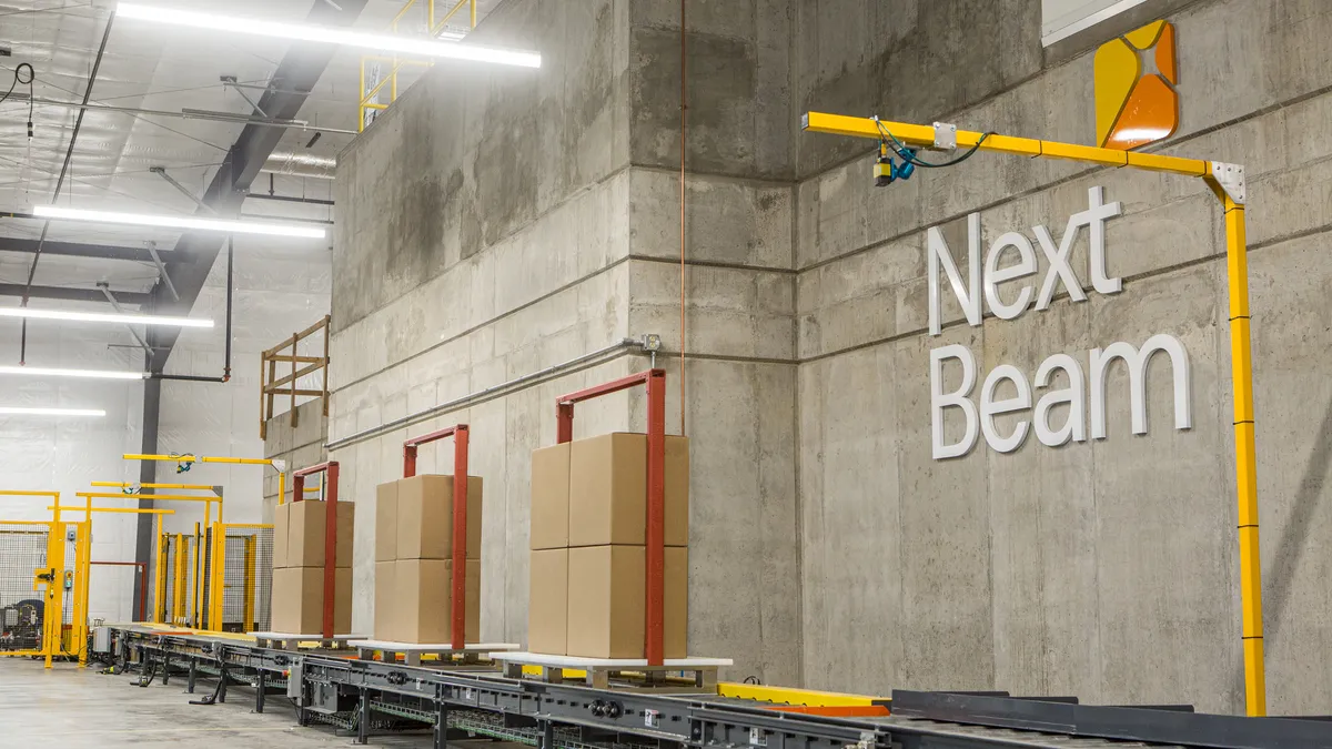 Boxes move on a conveyor belt next to a wall that says 'Next Beam'