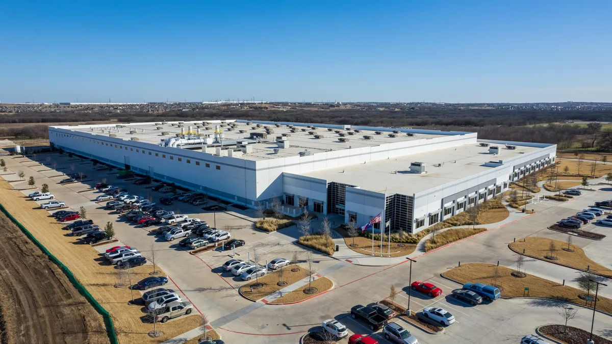 A large white building surrounded by cars on a parking lot on a sunny day.