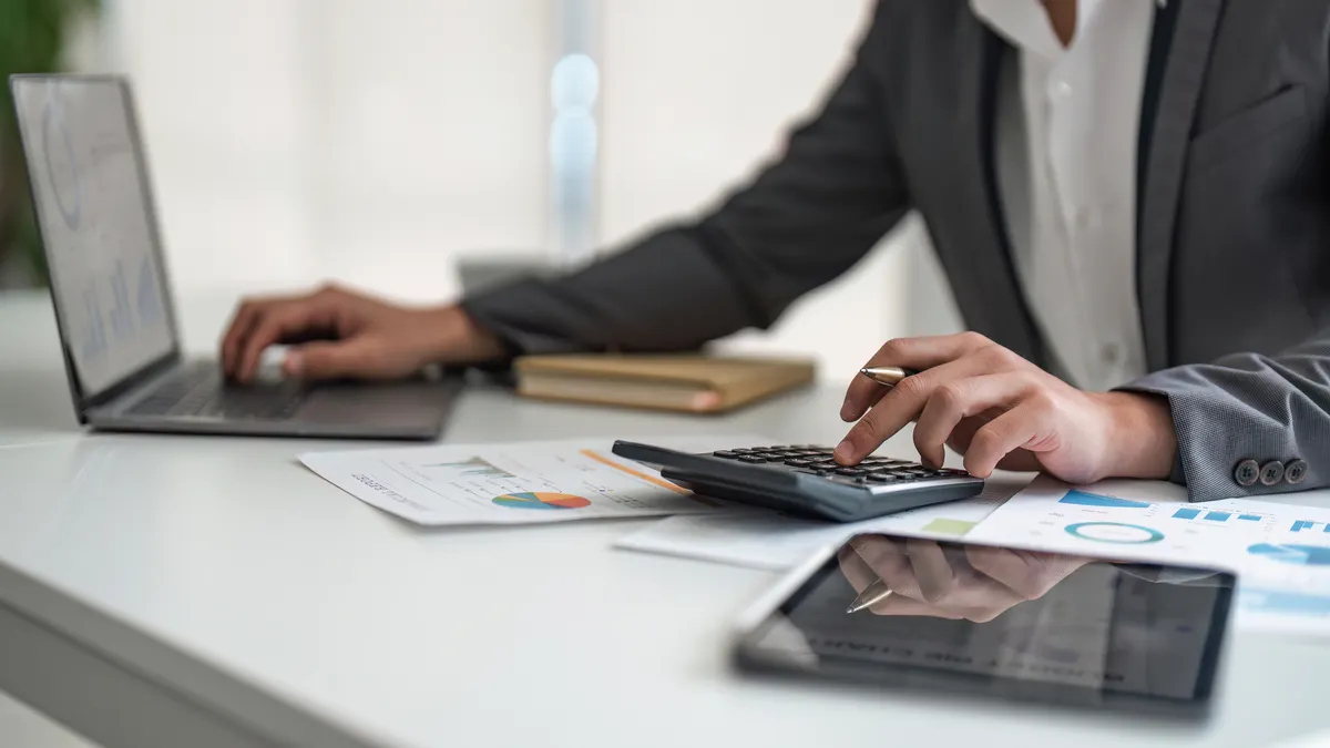 Person working at desk with laptop and calculator.