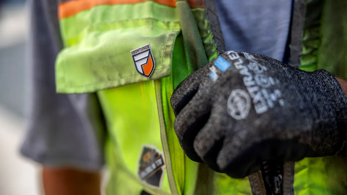 A close-up of a construction worker's vest with a pin on it.