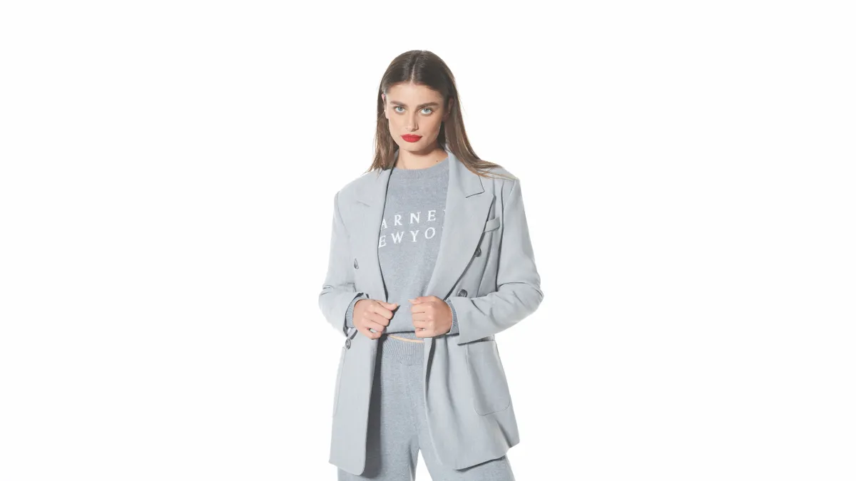 A person in a gray suit jacket and a gray sweater that reads "Barneys New York" looks at the camera.