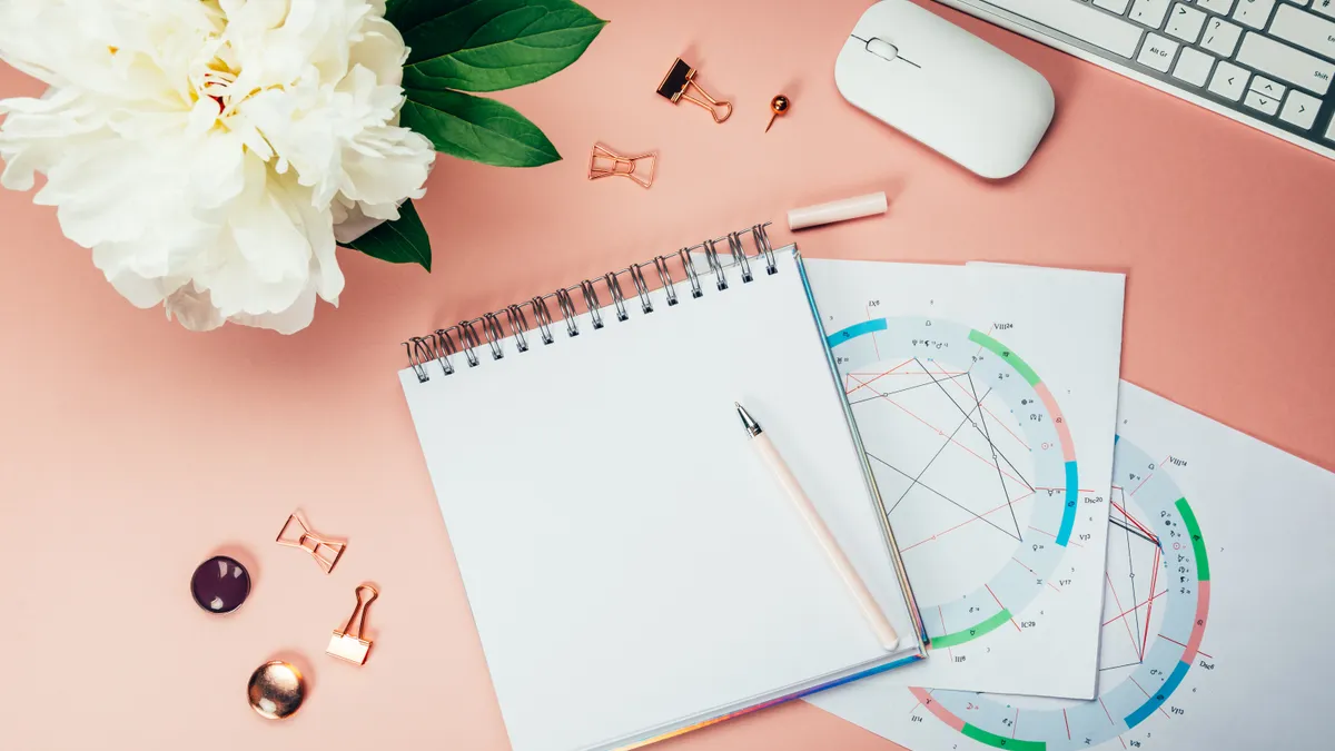 Open notebooks and astrological birth natal chart laying on pink background.