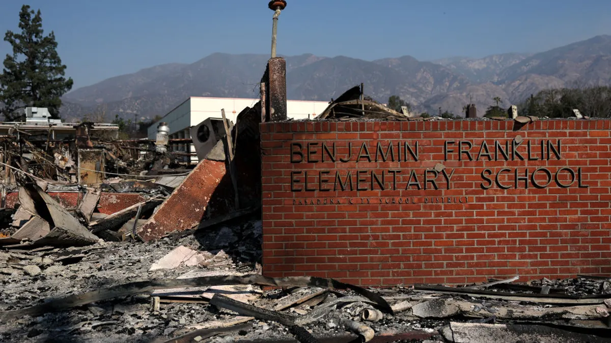 A brick wall with the name of an elementary stands among fire scorched landscape