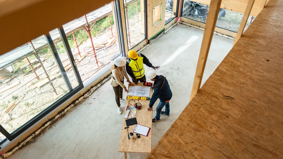 Team of one women architect and two men architects on a construction site. They are looking at blueprint. They are discussing about their project. Shot from above.