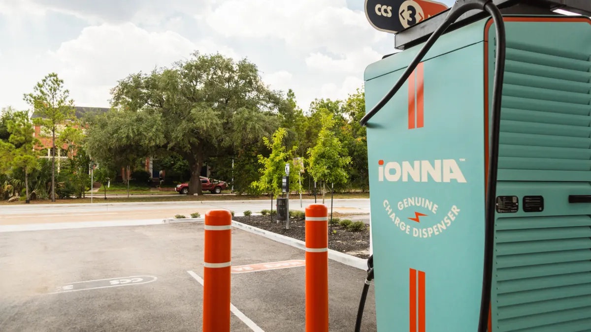 An Ionna-branded electric vehicle charger painted light blue and orange installed in a parking lot.