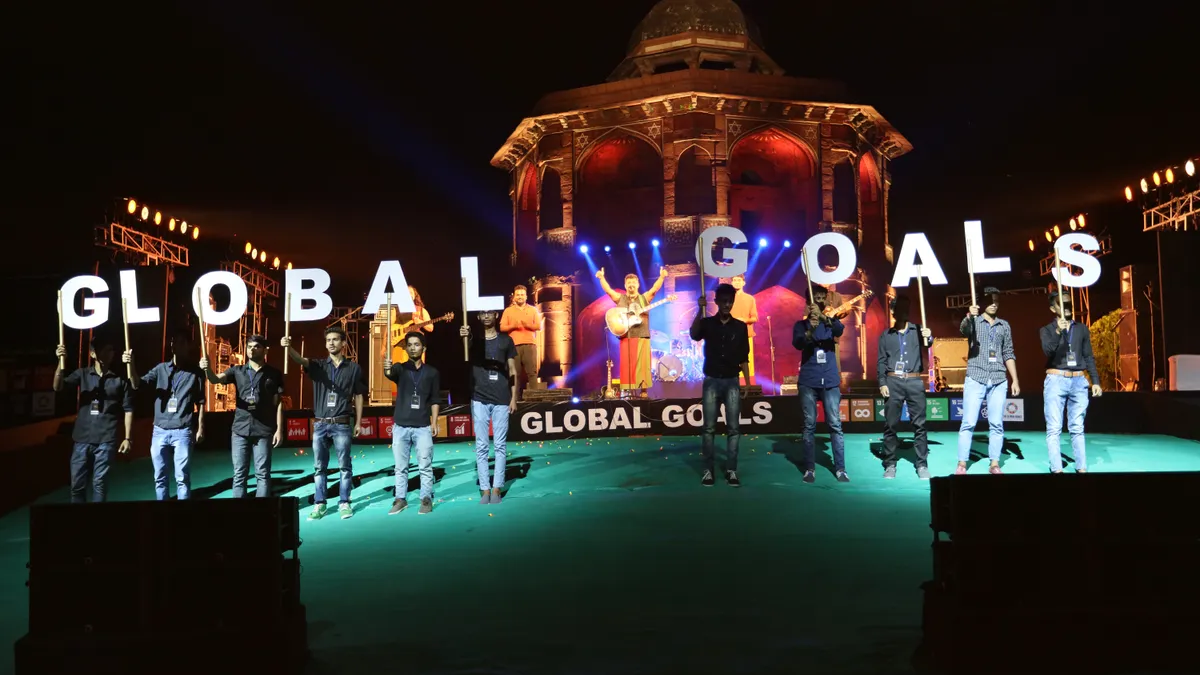 People stand on a green stage each holding one letter of the words Global Goals.