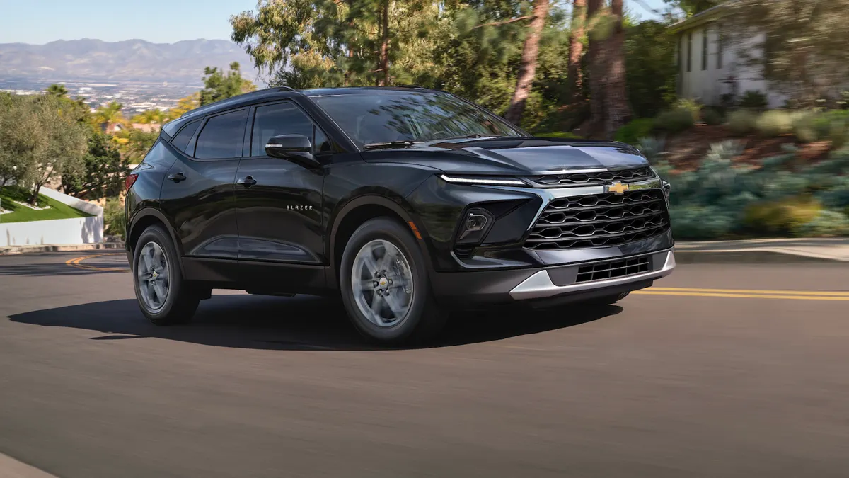 A dark gray 2025 Chevy Blazer SUV traveling on a road will mountains in the background.