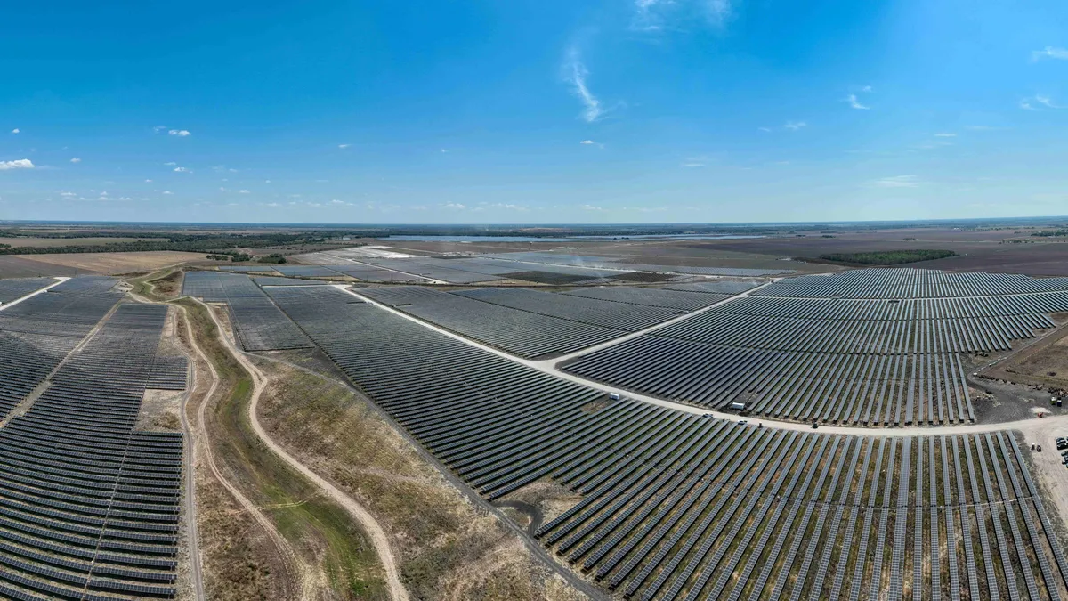 A field of solar panels across an arid landscape under a blue sky.