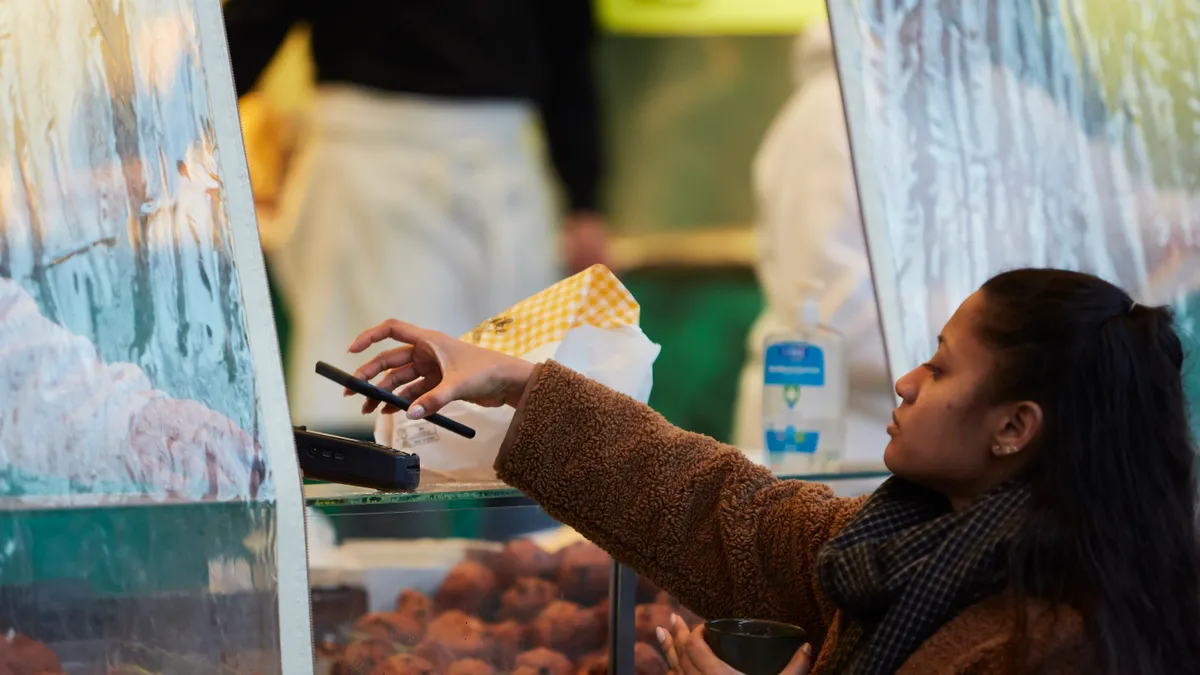 A client pays contactless with her smartphone as people queue up to buy deep fried doughnut balls (oliebollen) on December 31, 2020 in The Hague, Netherlands.