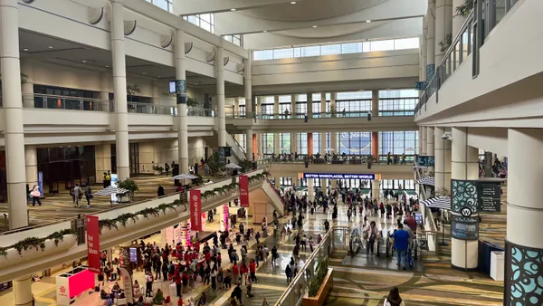 A crowd walks through a convention center, seen from a high vantage point.