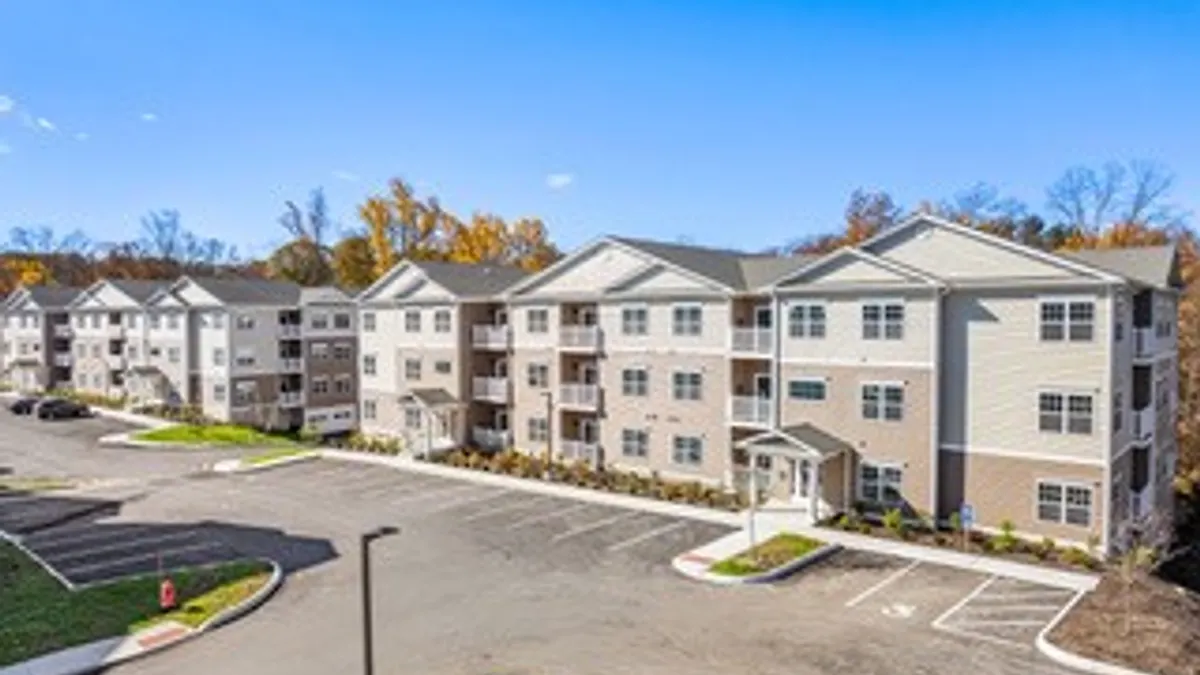 Three-level tan graden-style apartment property with a parking lot on the foreground