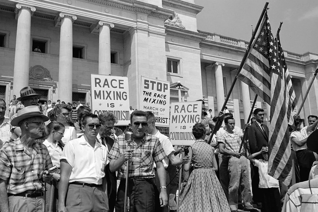 White protestors hold signs and flags standing outside of the Arkansas Capitol building