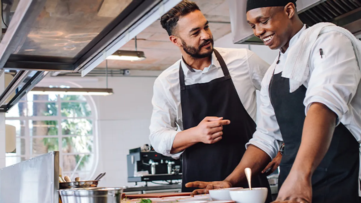 Two cooks making food dishes in restaurant kitchen.