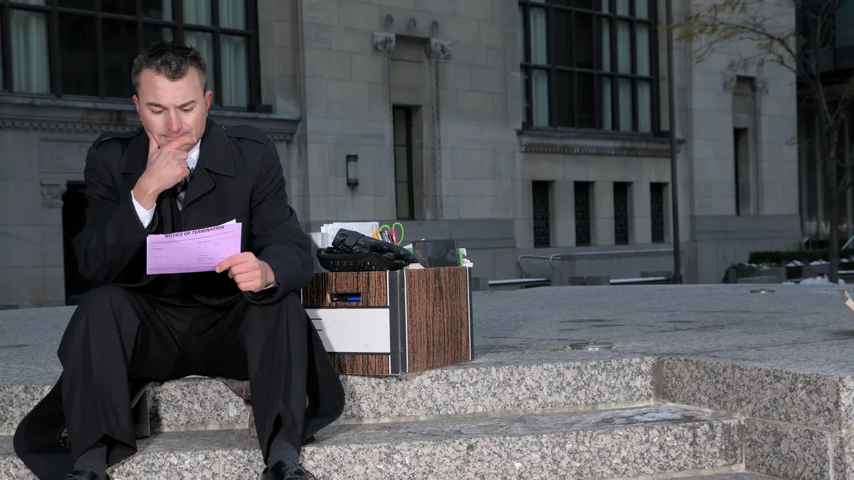 Businessman sitting on stairs with pink slip in hand.