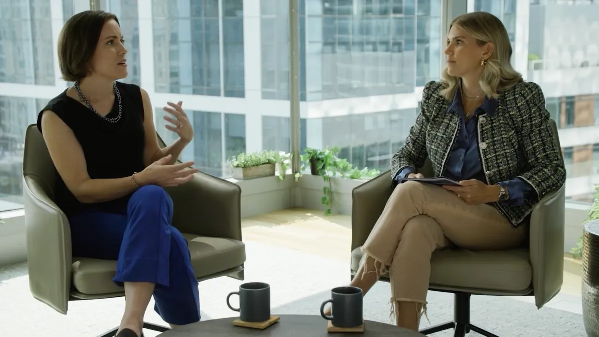 Two women, Emily Oster and Alyson Watson, sit across from each other in front of a large glass window.