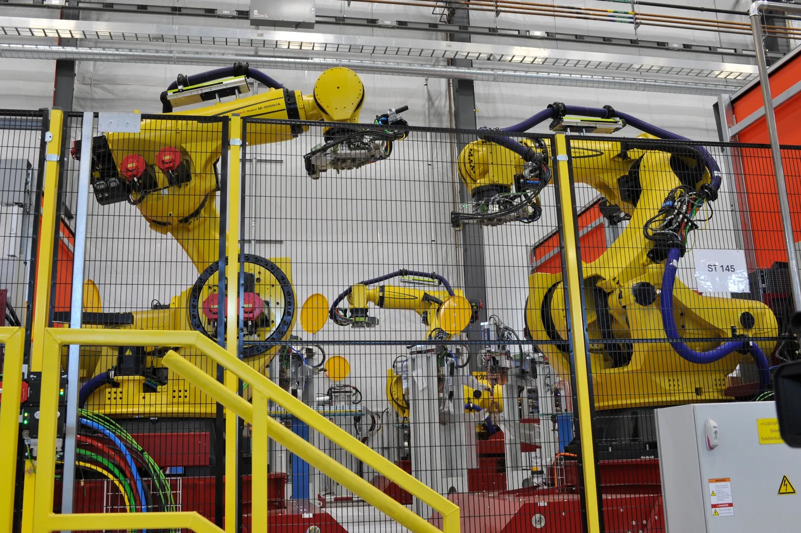 Industrial robots behind a mesh screen.