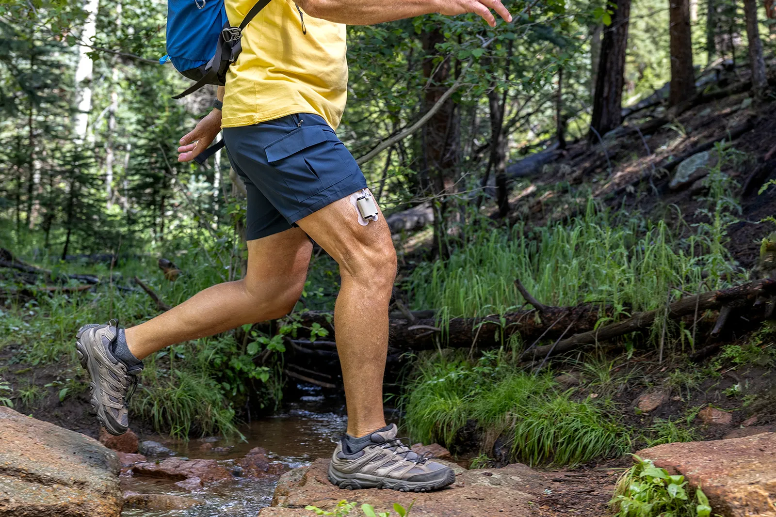 A person walks in a forest with a square device taped to their thigh.