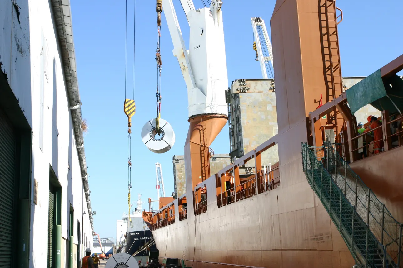 Longshoremen handle steel coils that are being offloaded from a vessel.