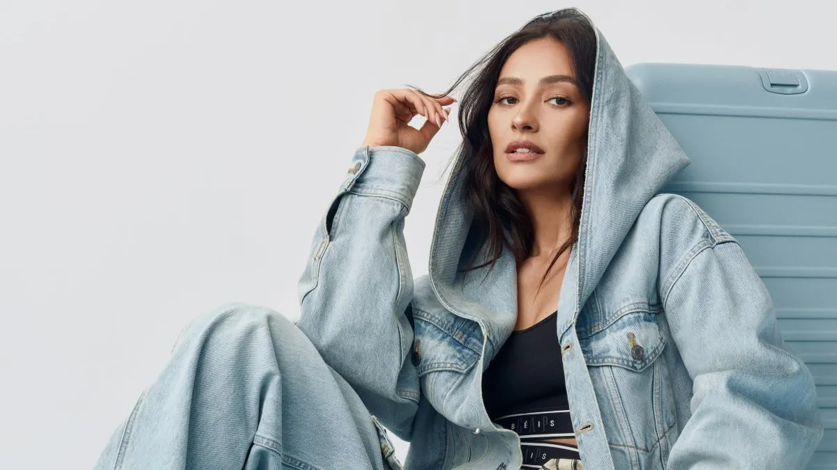 A model wears clothing from the Gap/Beis collection in front of luggage from the collection.