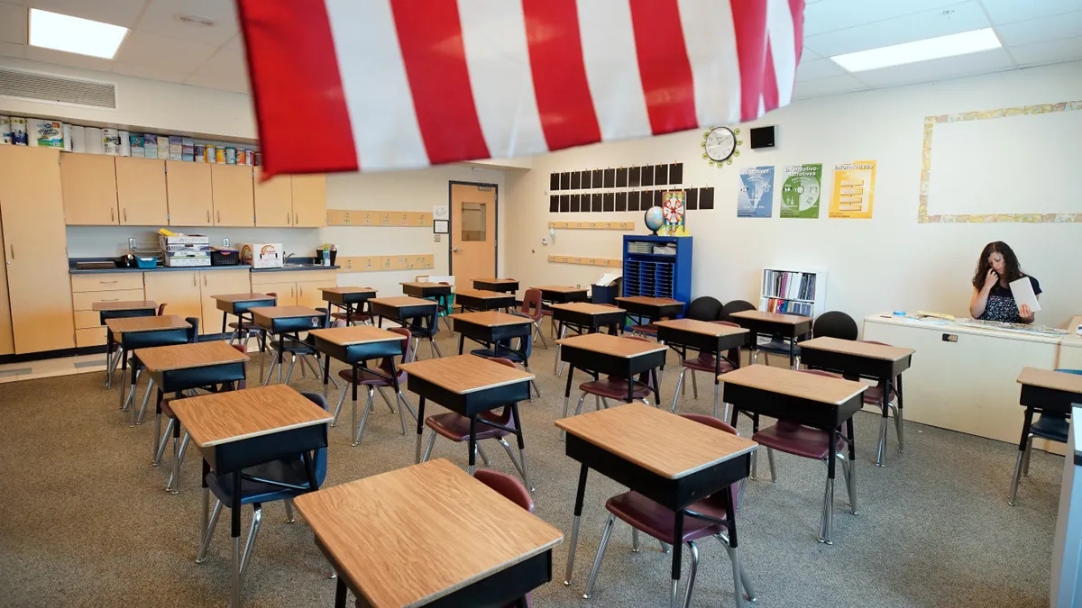 A teacher sits alone at her desk in an empty classroom as she prepares for students to return to its nigh-forgotten desks following COVID-19 closures.