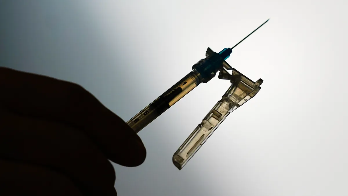 A silhouetted hand holds a syringe.