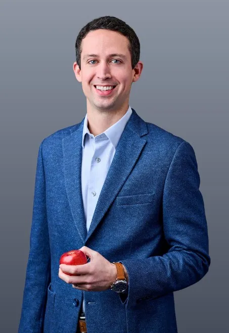 Headshot of a white man in a suit holding an apple