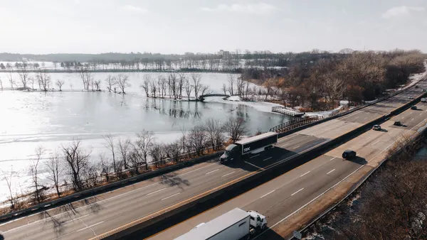 A Torc autonomous tractor-trailer on a three-lane highway near a body of water with snow covering parts of the landscape.