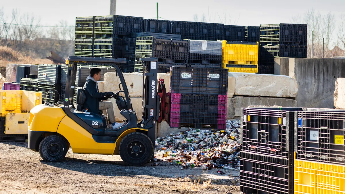 Person driving a forklift with container of glass for recycling