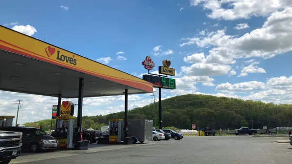 A photo of the forecourt of a gas station against the backdrop of forested hills. The canopy over the fuel pumps says "Loves" and road signs further out says "Love's" and "Arby's."