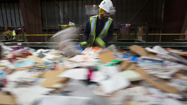 Person in hard hat and safety vest stands over fast-moving conveyor belt with recyclables in Oregon