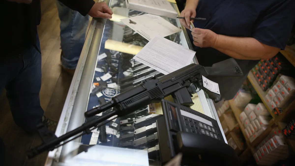 Rifle on counter at gun store with hands of two people showing an apparent transaction.