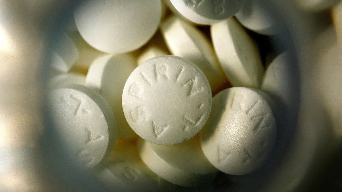 A top-down shot of round aspirin pills in a clear plastic bottle.