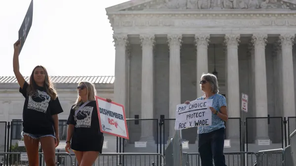 An abortion rights activist stands next to anti-abortion rights activists in front of the U.S. Supreme Court Building, which is surrounded by fencing.